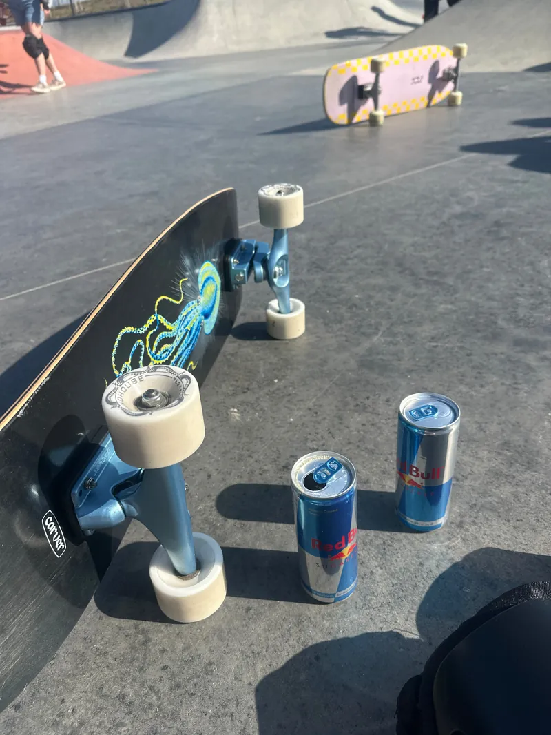 A Carver surfskate resting at a skatepark beside two Red Bull cans.