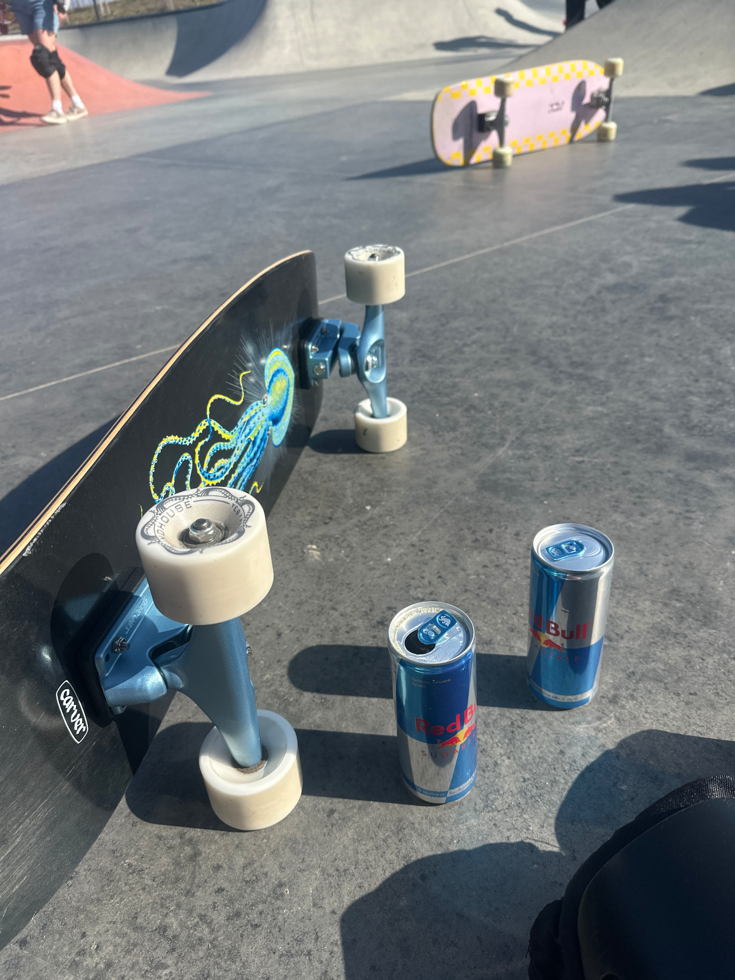 A Carver surfskate resting at a skatepark beside two Red Bull cans.